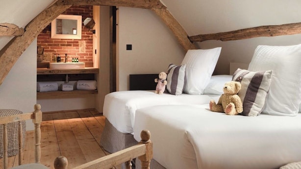 Een gezellig slaapkamer onder de dakpannen met zichtbare houten balken, een ingebouwde bakstenen muur, een groot bed met kussens en een teddybeer.