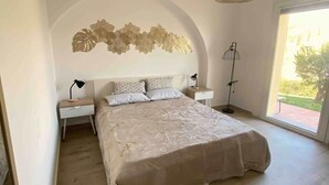 Une chambre avec un grand lit, un luminaire fixé au mur et une vue par la fenêtre.