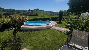Un jardin avec une piscine, une terrasse avec des chaises et une vue sur des collines ondoyantes.