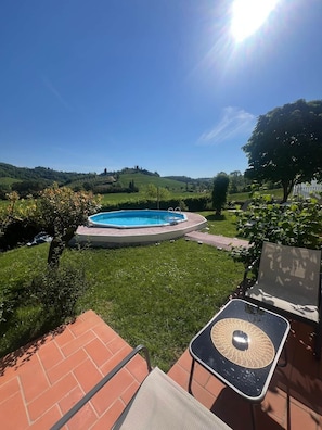 Un giardino sul retro con piscina, un patio con sedie e vista su dolci colline.