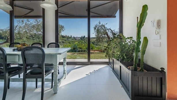 Un área de comedor al aire libre con una mesa y sillas, vista a zonas verdes y edificios, y una planta de cactus.