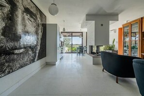 Un interno moderno con un'ampia opera d'arte astratta a parete, un divano nero e una zona pranzo illuminata dalla luce naturale.