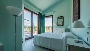 Un dormitorio con cama, escritorio, lámpara, espejo y vista al exterior.