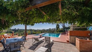 Un área junto a la piscina con mesa y sillas, un espacio de descanso cubierto y vistas al paisaje.