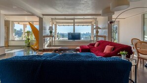 Uma sala de estar moderna com uma janela grande, um sofá vermelho, um cobertor azul e uma escada.