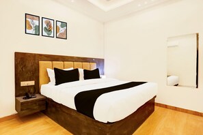 A modern hotel room with a large bed, a wooden headboard, a bedside table with a phone, and three framed artworks on the wall. - Super Deluxe Room OYO Balua Road (Varanasi)