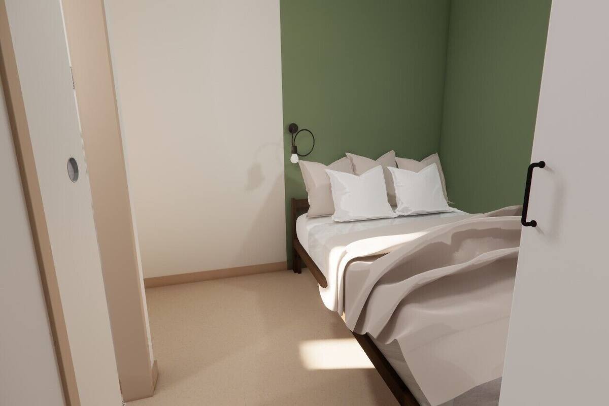 A bedroom with a bed, pillows, and a wall-mounted light fixture.