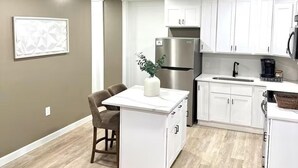 A modern kitchen with white cabinets, a stainless steel refrigerator, a dining area with a table and chairs, and a light-colored wooden floor. - Walk to DPAC + Bulls - Chic Downtown Durham condo (Durham)