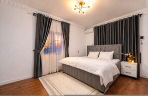 Ein Schlafzimmer mit Bett, Nachttisch, Vorhängen und einer Deckenleuchte.