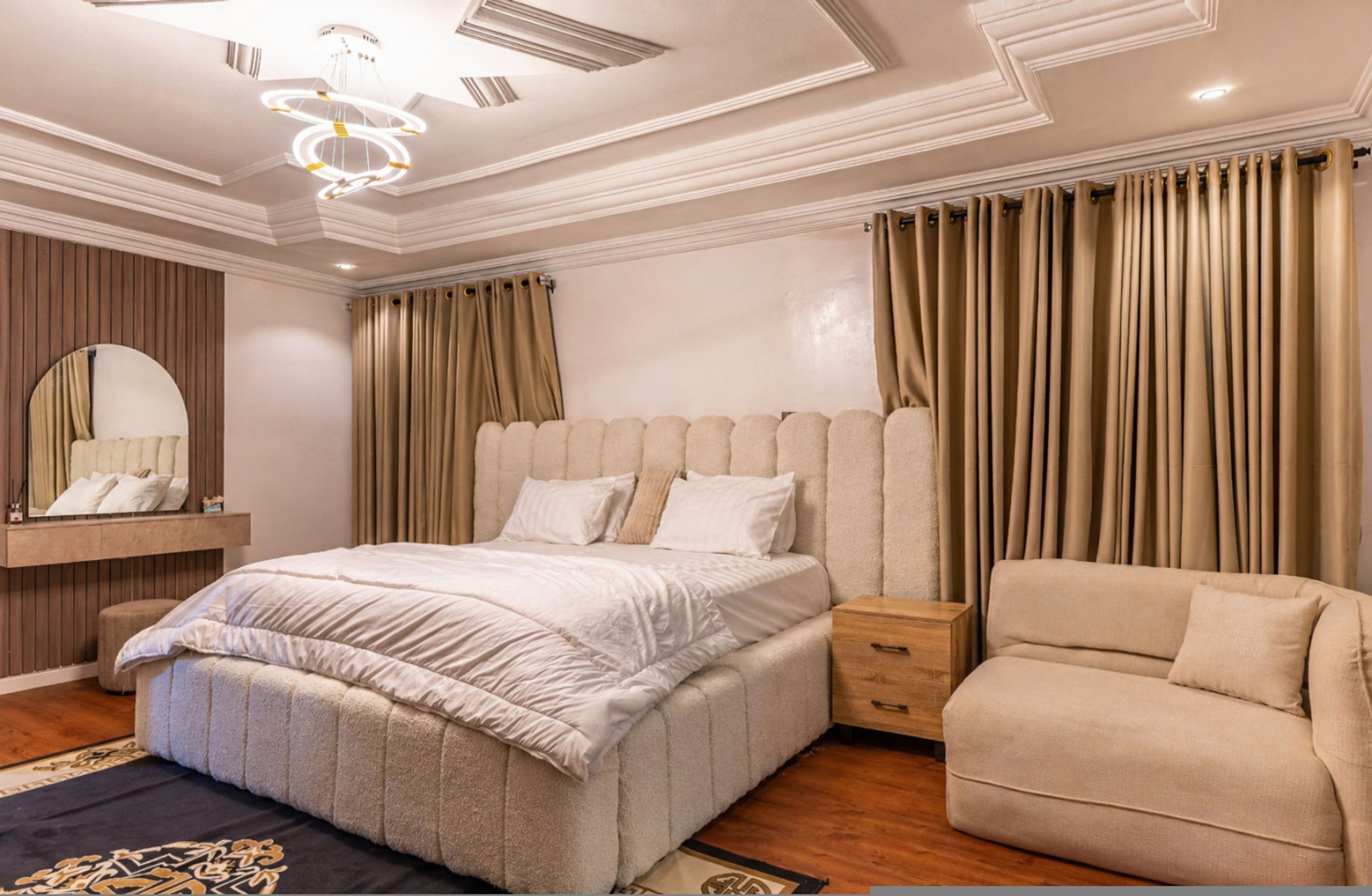 A bedroom with a large bed, a bedside table, a chair, a mirror, and curtains.