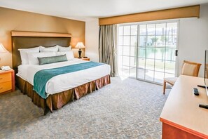 Ein Hotelzimmer mit einem großen Bett, einem Schreibtisch, einem Sessel, einem Nachttisch und Blick ins Freie.