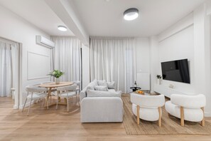 Ein modernes Wohnzimmer mit einer Couch, Sesseln, einem Esstisch und einem Fernseher.