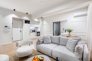 Ein modernes Wohnzimmer mit einem grauen Sofa, einem runden Couchtisch mit Früchten und einer Küche im Hintergrund.
