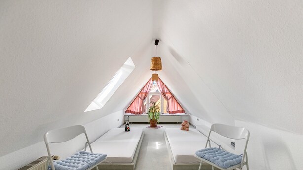 A room with a sloped ceiling, two white foldable chairs with blue cushions, a small potted plant, and a window with red curtains. - Apartment '3-Room Palmyra' with Balcony, Wi-Fi and Shared Garden (Büsum)