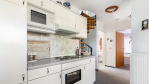 A kitchen with white cabinets, a stove, and a microwave. There is a staircase leading to another level. - Apartment '3-Room Palmyra' with Balcony, Wi-Fi and Shared Garden (Büsum)