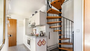 A compact kitchen with white cabinets, a stove, and a wooden spiral staircase. - Apartment '3-Room Palmyra' with Balcony, Wi-Fi and Shared Garden (Büsum)