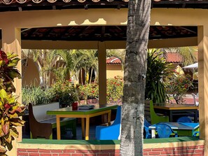 A covered outdoor area with a brick wall, a palm tree, and colorful play structures. - Porto Belo Park (Porto Seguro)