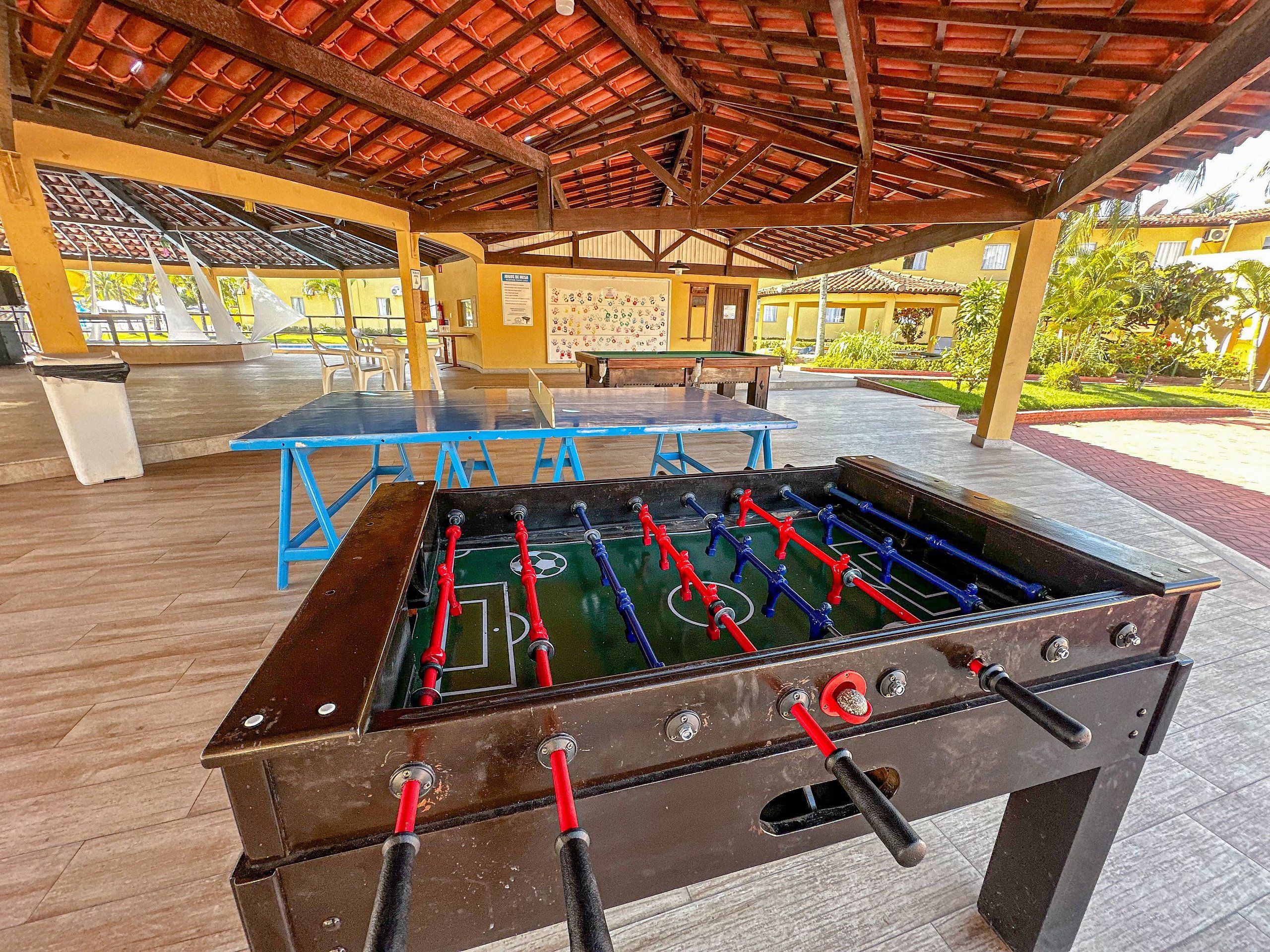 A foosball table in a covered outdoor area with tables and chairs in the background.
