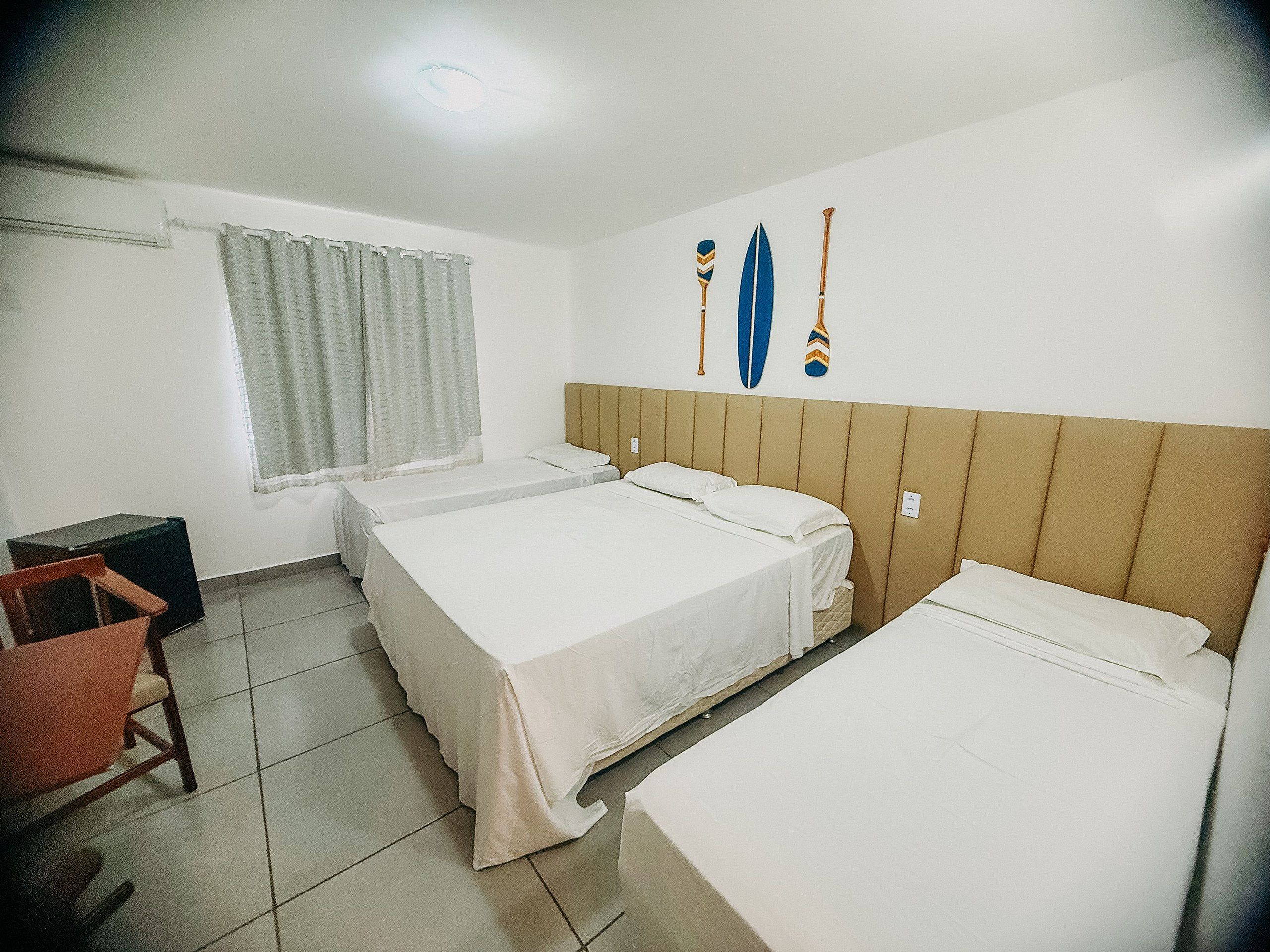Una camera d'albergo con due letti, una finestra con tende, una scrivania e una sedia.