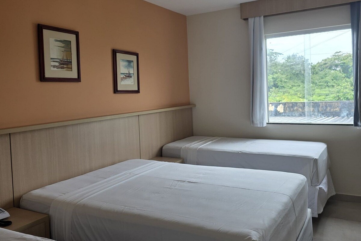 Habitación de hotel con dos camas, ventana con vistas y dos cuadros en la pared.