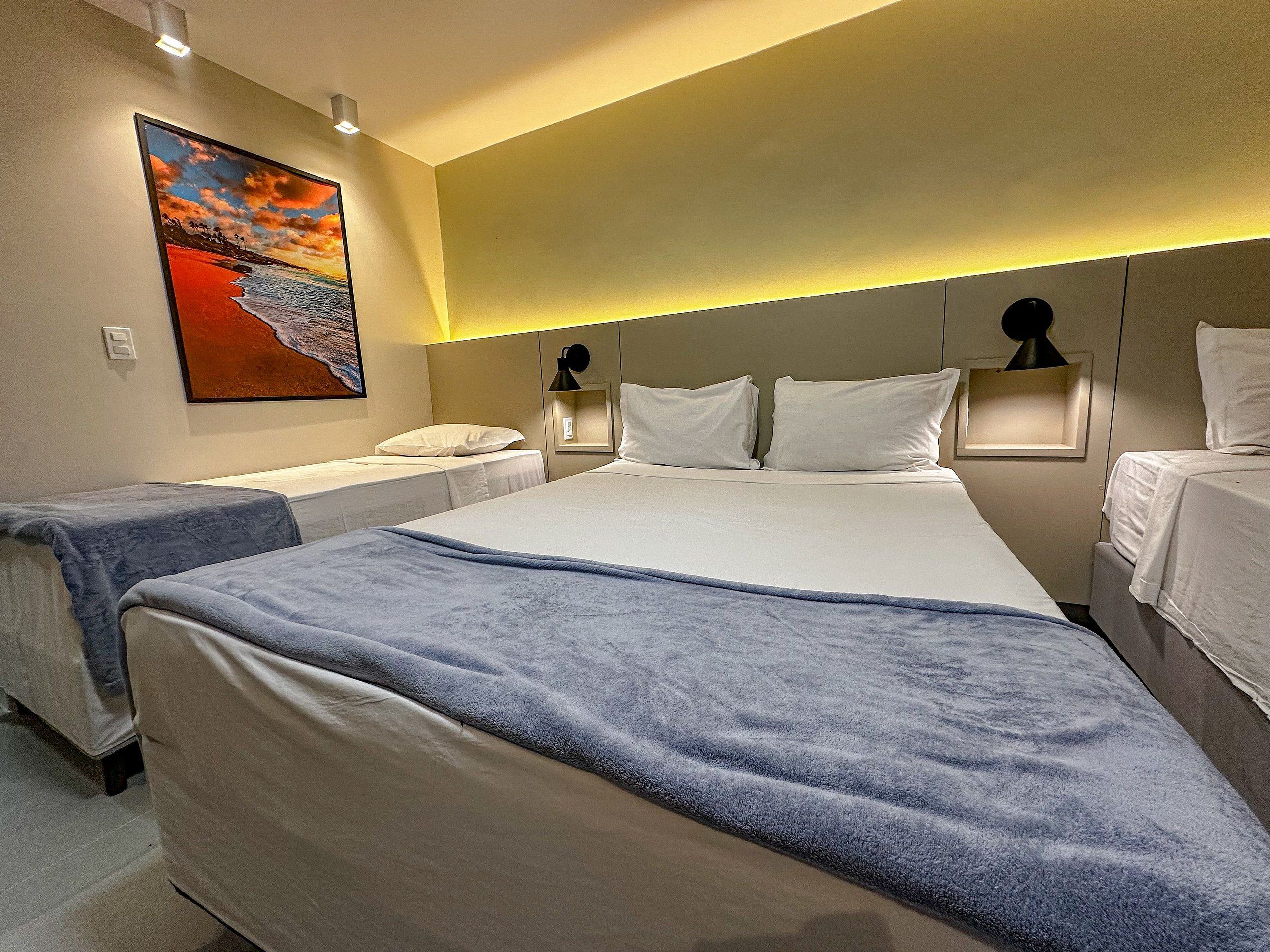 A hotel room with a large bed, two bedside tables with lamps, a painting on the wall, and a view of the sea.