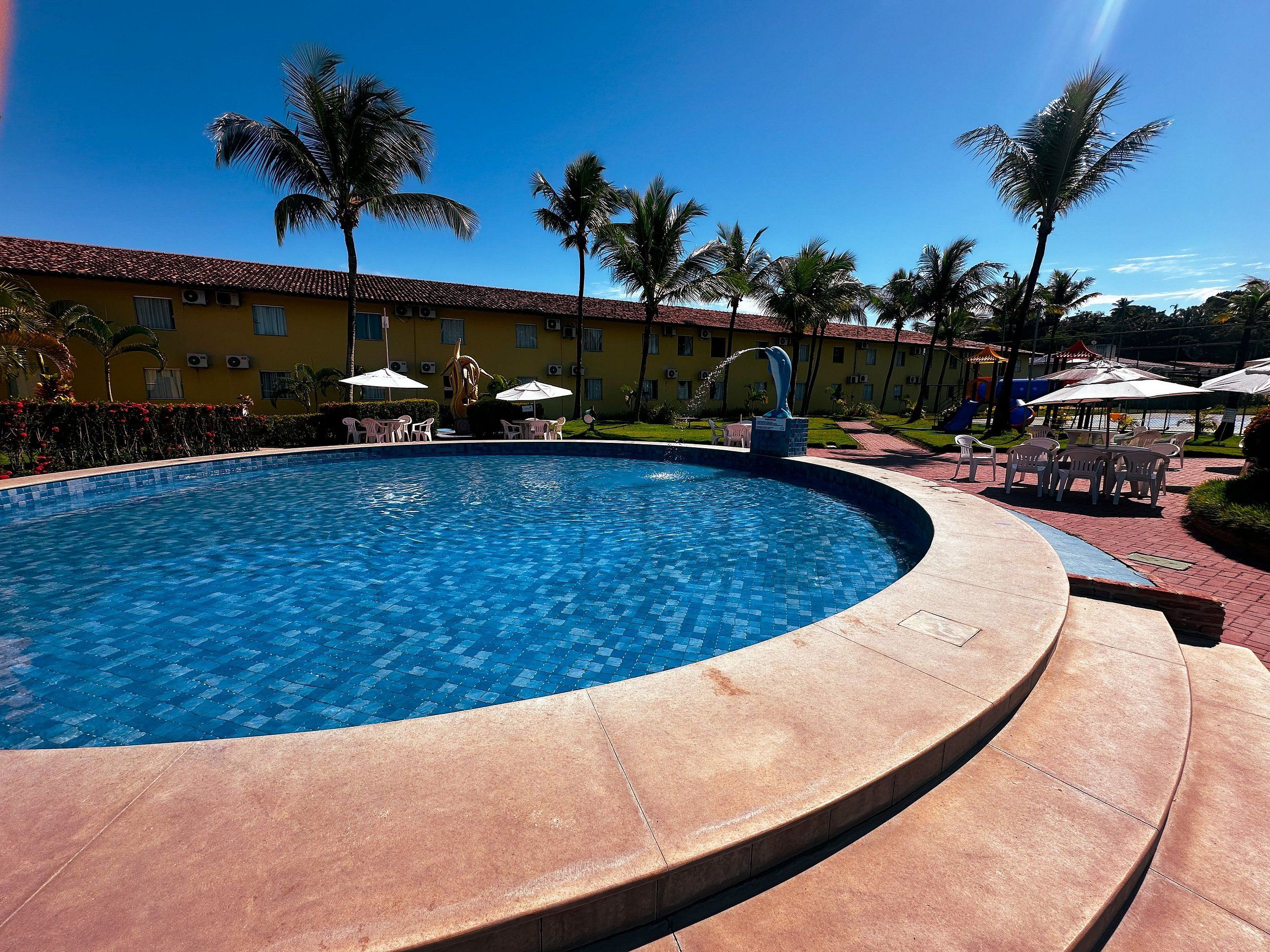 A swimming pool with a tiled edge, surrounded by palm trees and outdoor seating.