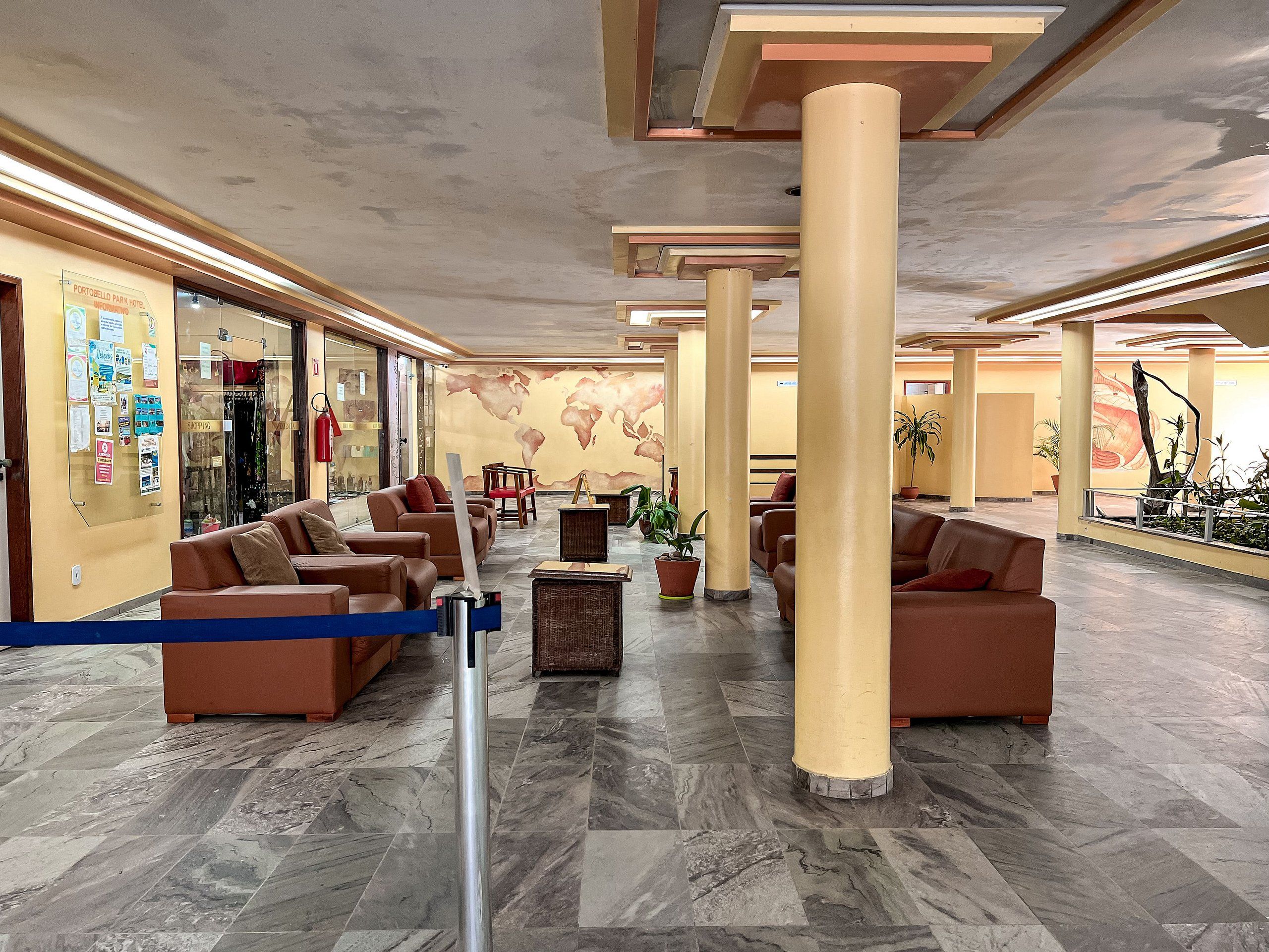 A hotel lobby with seating areas, a world map mural, and a glass storefront.