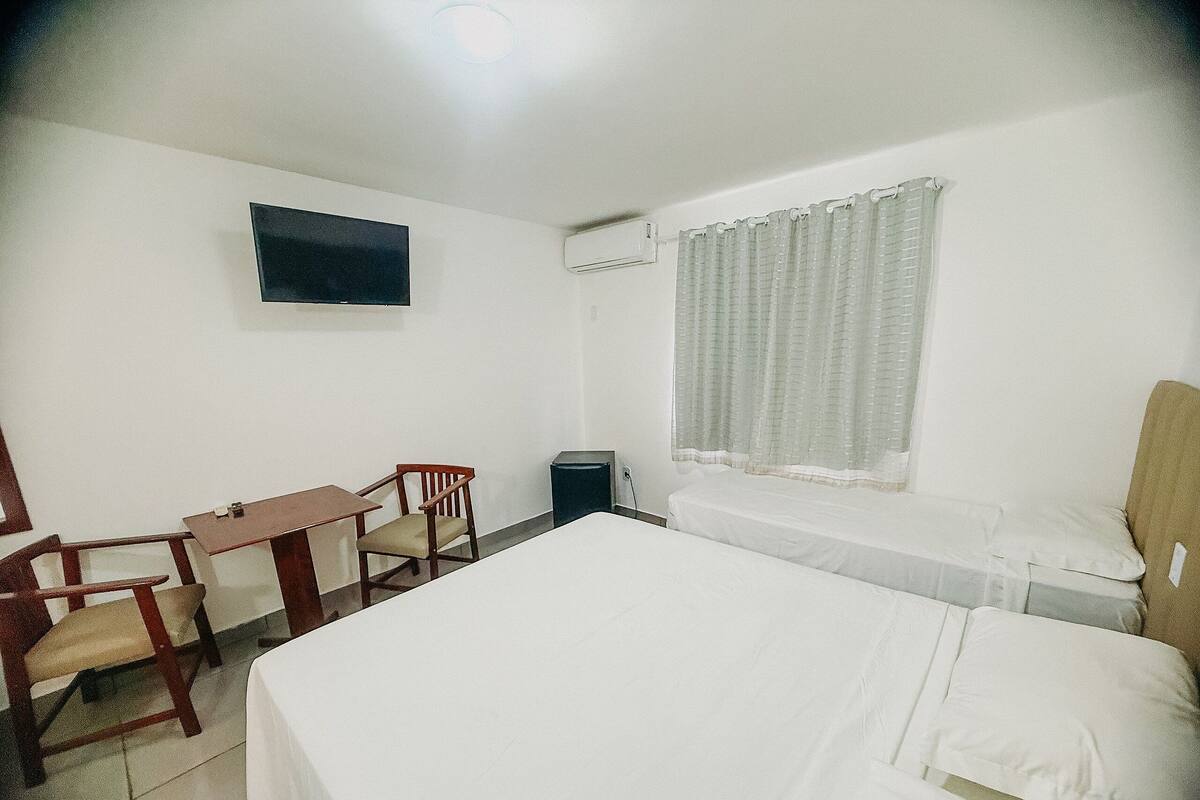 Um quarto com cama, escrivaninha, cadeira, televisão e ar-condicionado.