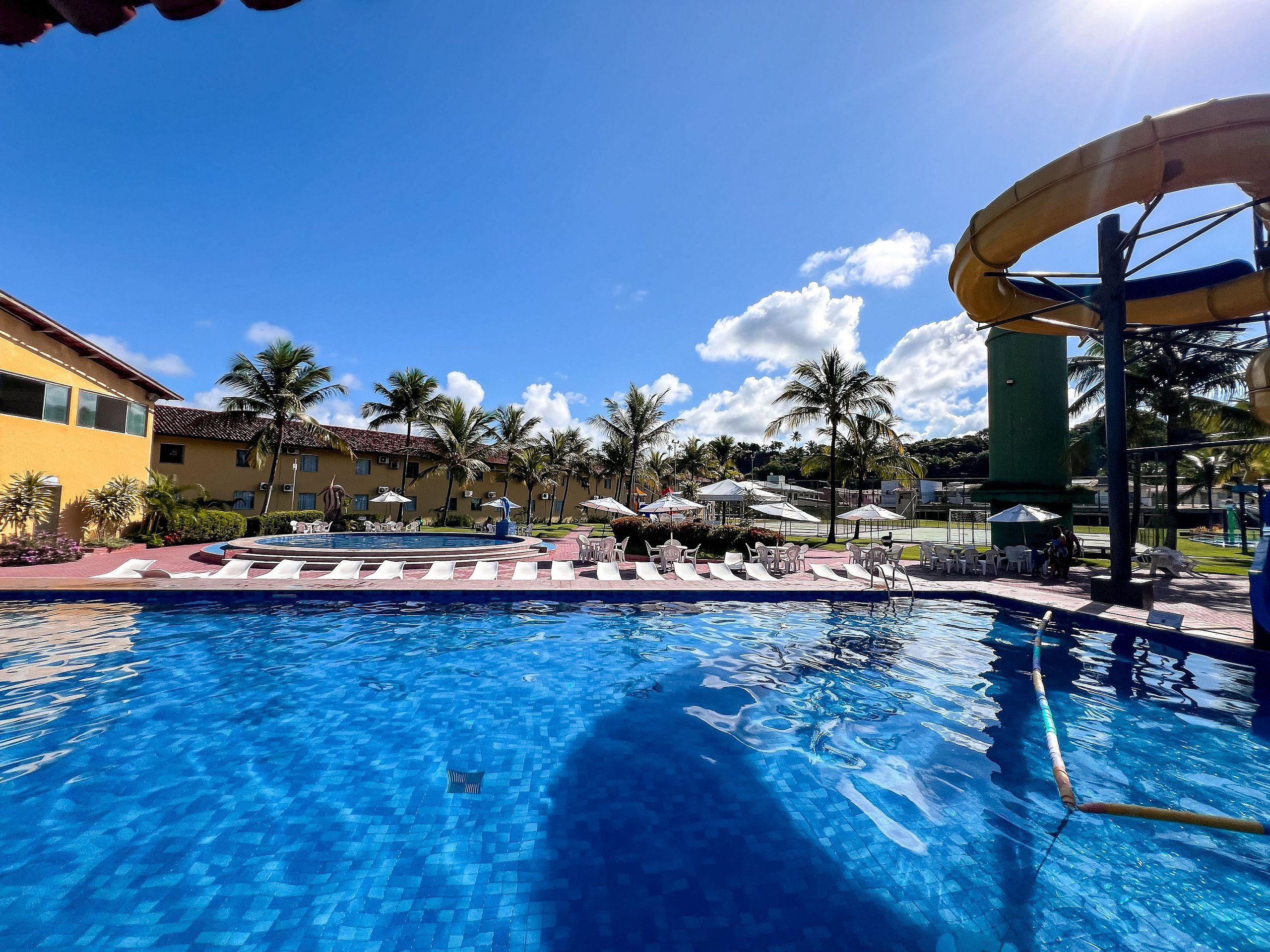 A swimming pool with lounge chairs, a water slide, and palm trees.