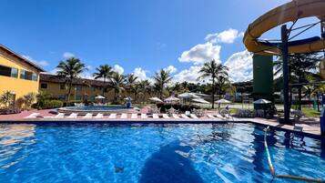 A swimming pool with lounge chairs, a water slide, and palm trees.