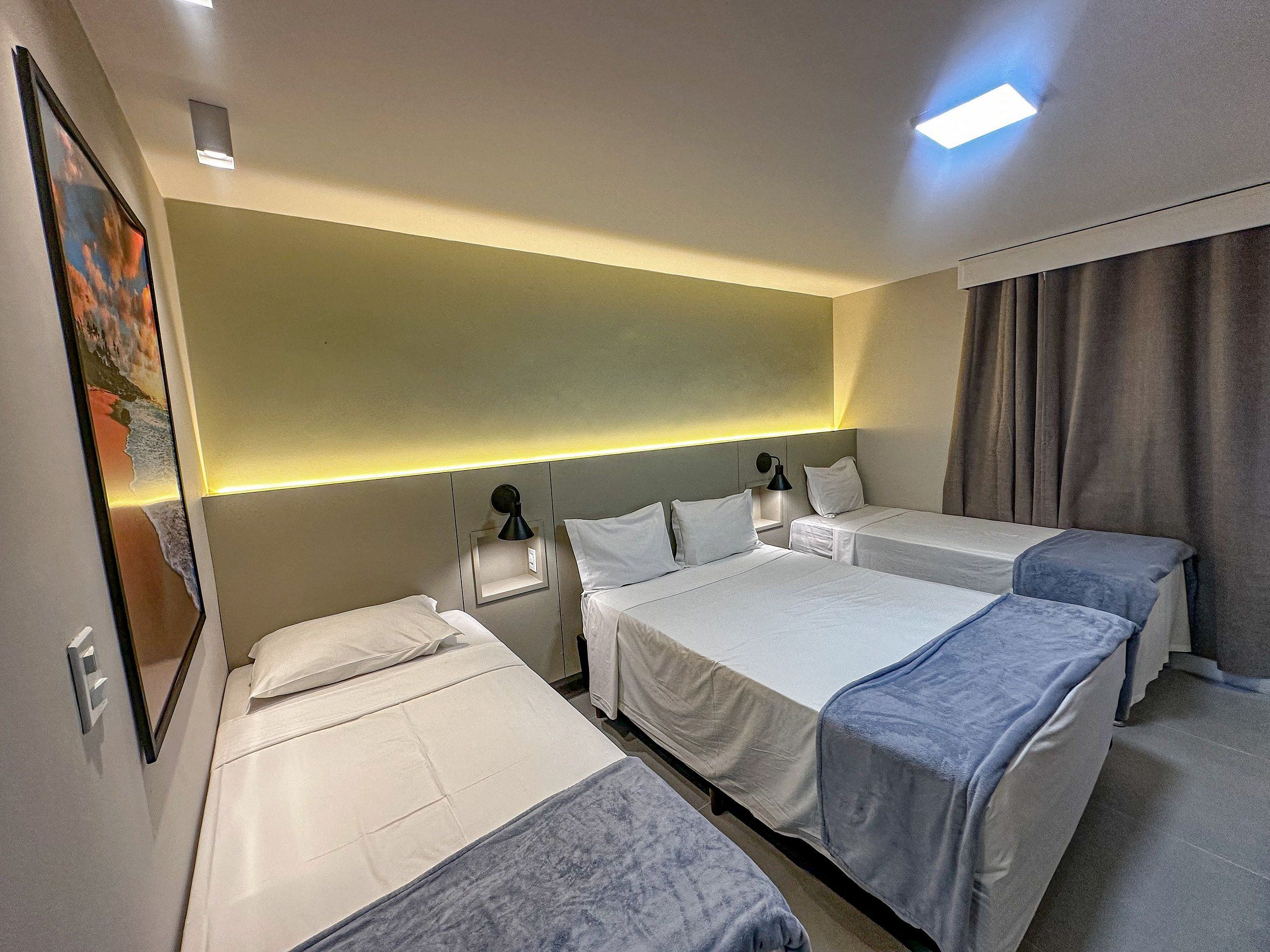 A hotel room with two single beds, a nightstand with a lamp, and a painting on the wall.