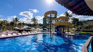 A swimming pool with water slides, lounge chairs, and umbrellas.