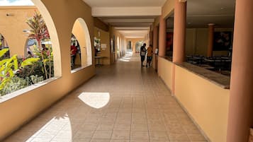 A corridor with tiled flooring, arches, and a view of a restaurant area.