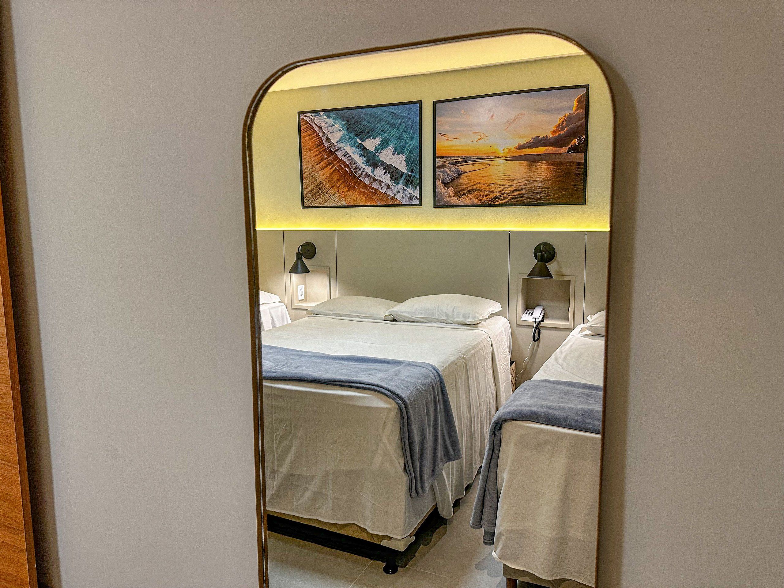 Quarto de hotel com duas camas, uma mesa de cabeceira com abajur e um telefone fixado na parede.