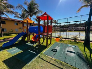 A playground with slides and a climbing structure, surrounded by a fence and palm trees. - Porto Belo Park (Porto Seguro)