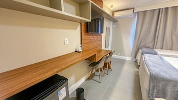 A hotel room with a bed, a desk with chairs, a television, and a small refrigerator.
