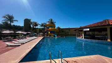 A swimming pool with a water slide, lounge chairs, and umbrellas.