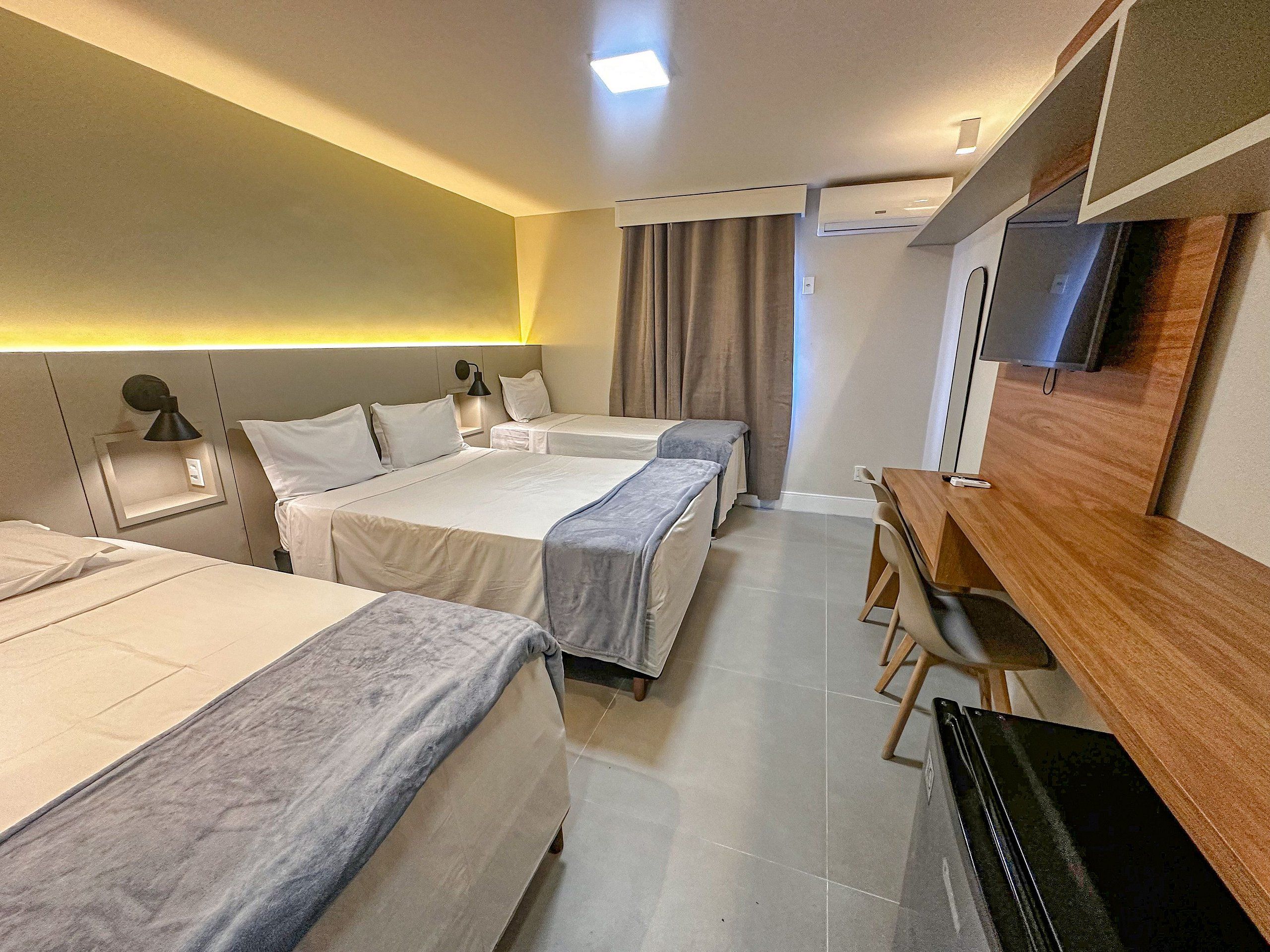 Habitación de hotel con dos camas, un escritorio, un televisor y aire acondicionado instalado en la pared.