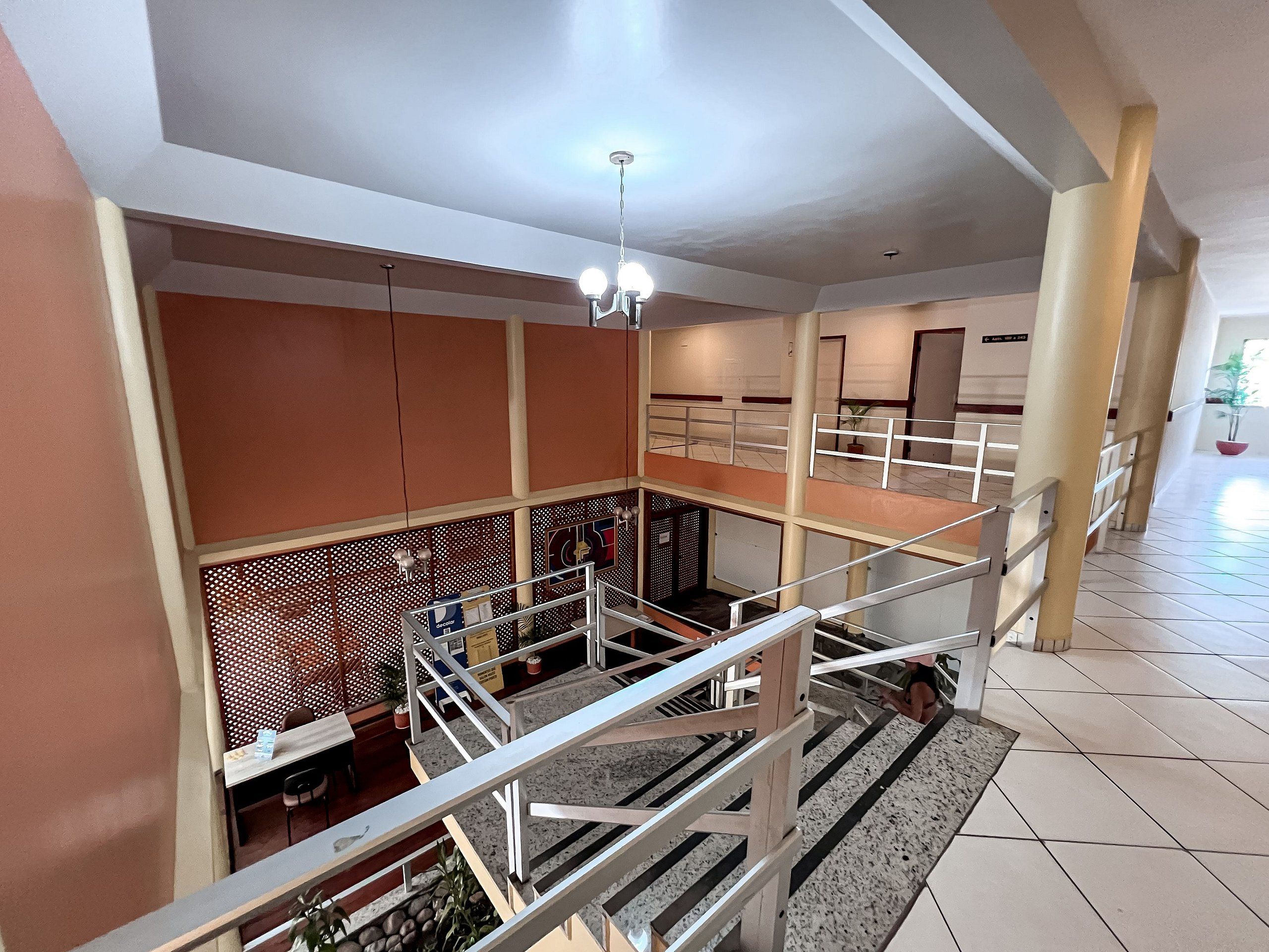 Interior com vários níveis, escada, corrimão e luminária no teto.