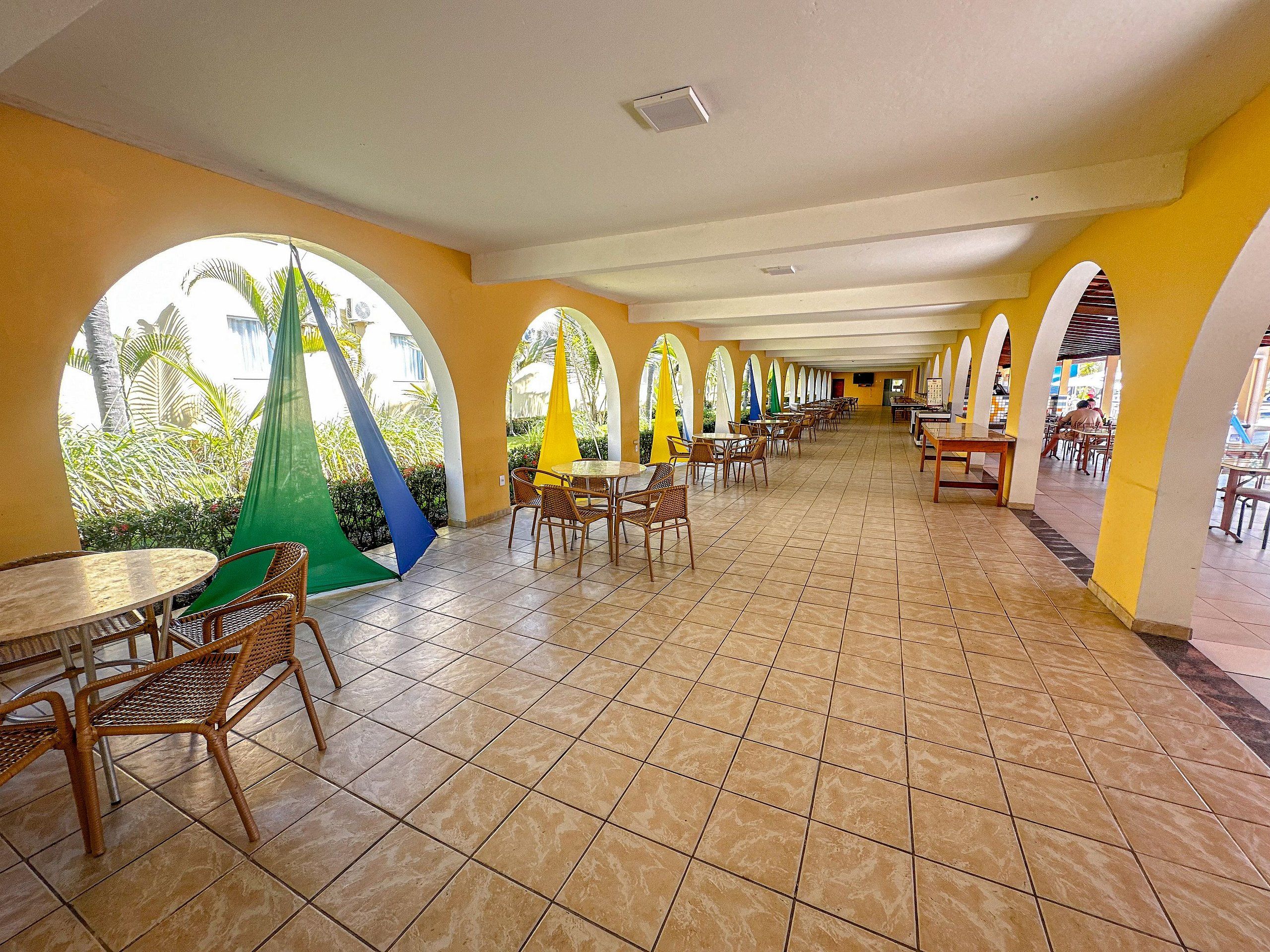 A spacious indoor dining area with multiple tables and chairs, arched ceiling, and a view of greenery outside.