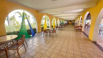 A spacious indoor dining area with multiple tables and chairs, arched ceiling, and a view of greenery outside.