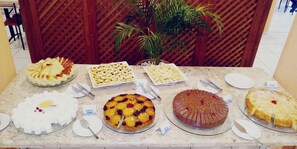 A buffet table with various desserts and a plant in the background. - Porto Belo Park (Porto Seguro)