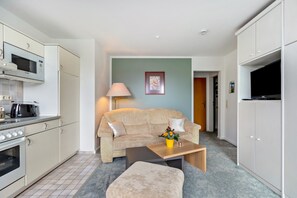Ein kompakter Wohnbereich mit Küchenzeile, einer Couch, einem Couchtisch und einem Fernseher.