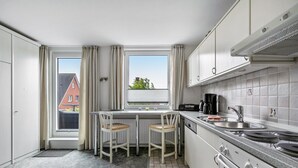 Pieni, käytännöllinen keittiö, jossa on ikkuna, kaksi baarijakkaraa, liesi ja pesuallas.