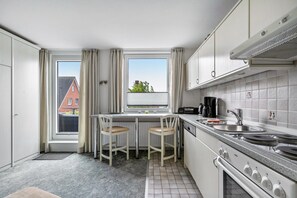 Una cocina compacta con ventana, dos taburetes, estufa y pileta.