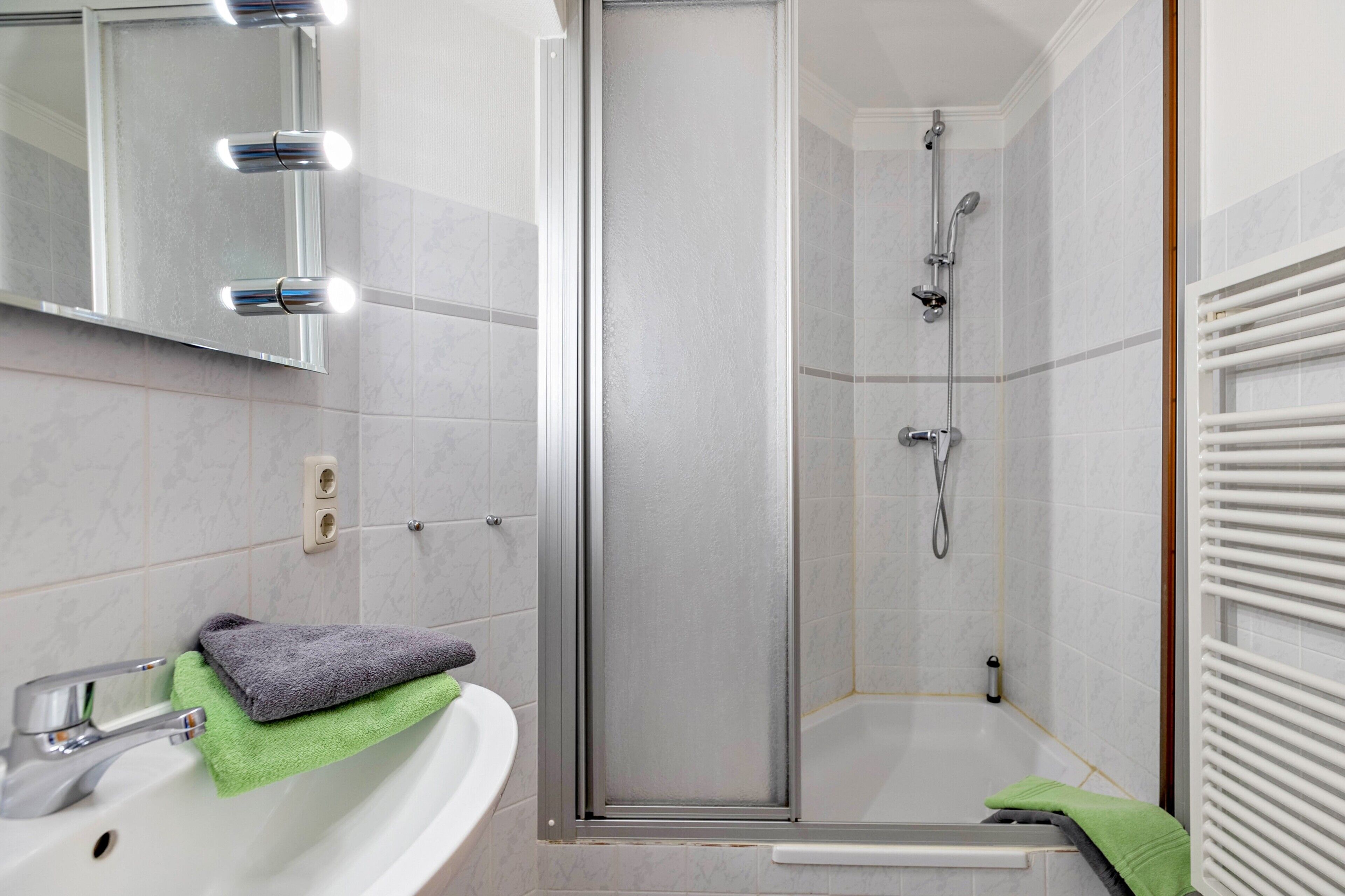 A bathroom with a shower, a sink, and a mirror with lights.