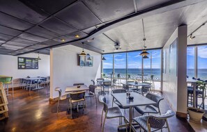Ein Restaurant mit Blick auf den Ozean, ausgestattet mit Tischen, Stühlen, einer Speisekarte und Pendelleuchten.