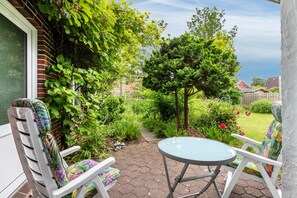 Eine Terrasse mit zwei Stühlen und einem Tisch, umgeben von Pflanzen und einer Ziegelwand.