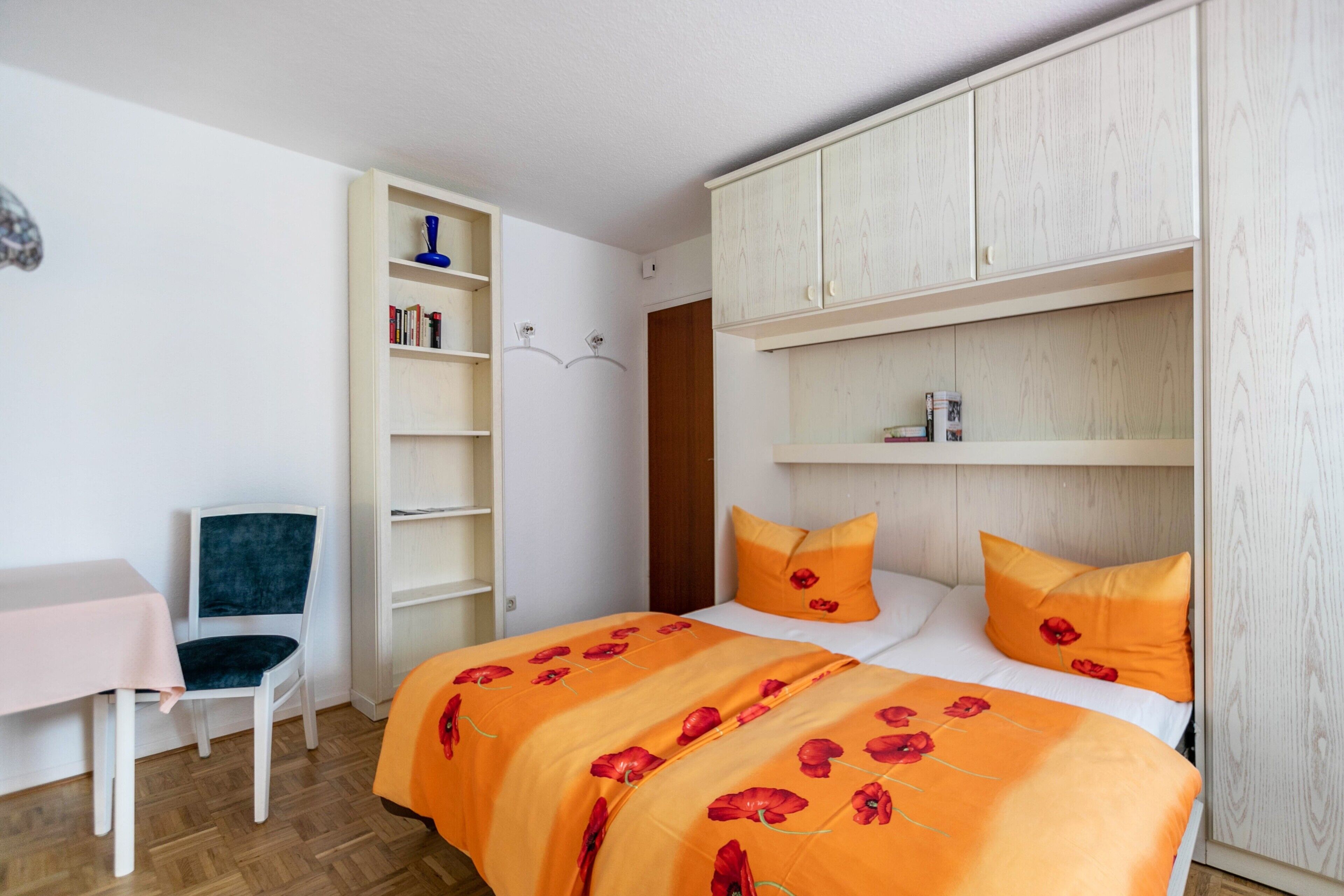 Een slaapkamer met een bed, een stoel, een klein tafeltje en een kledingkast.