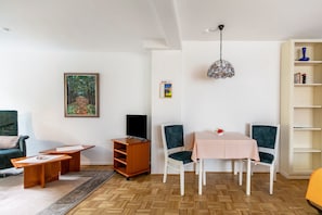 Un salon comprenant un canapé, une table basse, un meuble pour la télévision, une table à manger avec des chaises, une bibliothèque et un luminaire suspendu.
